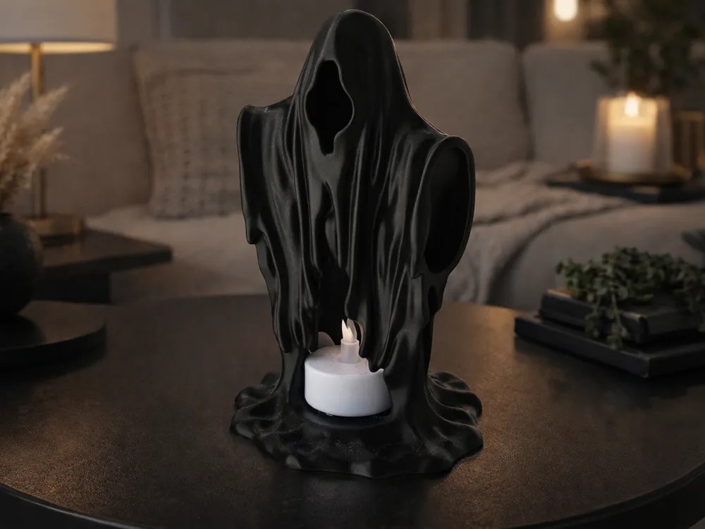 Draped black ghost tealight holder with a lit LED tealight at its base, on a living room table, 3D printed